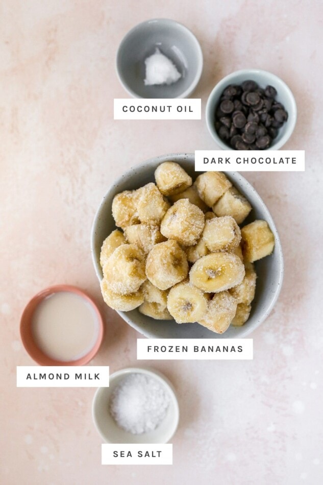 Coconut oil, dark chocolate chips, frozen banana, almond milk and sea salt measured out in bowls.