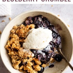 Blueberry crumble topped with vanilla ice cream in a bowl with a spoon.