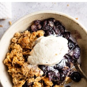 Blueberry crumble topped with vanilla ice cream in a bowl with a spoon.