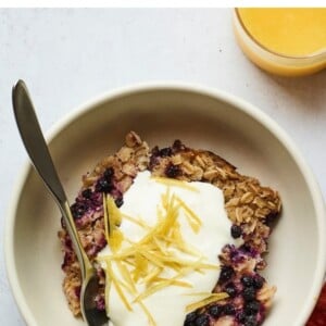Serving of blueberry lemon baked oatmeal in a bowl and topped with yogurt and lemon zest.