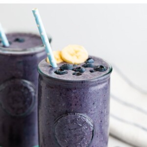 Blueberry smoothie topped with blueberries, banana and a straw.