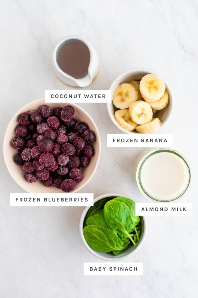 Coconut water, frozen banana, frozen blueberries, almond milk and baby spinach measured out in bowls.