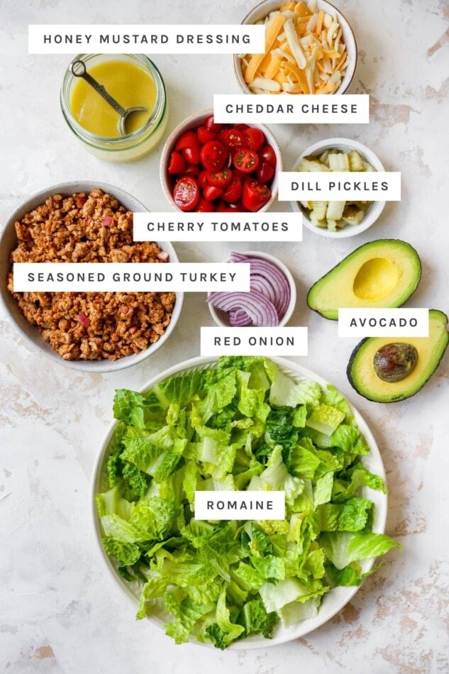 Ingredients measured out to make a cheeseburger salad, including cheese, veggies, romaine, ground turkey and honey mustard dressing.