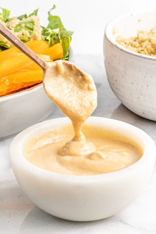 Spoon drizzling citrus tahini dressing from a bowl.
