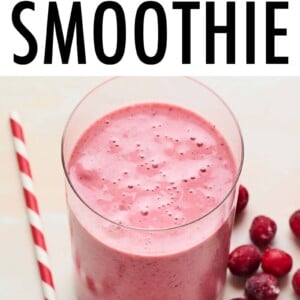 Glass with cranberry smoothie. A white and red paper straw and frozen cranberries are next to the glass.