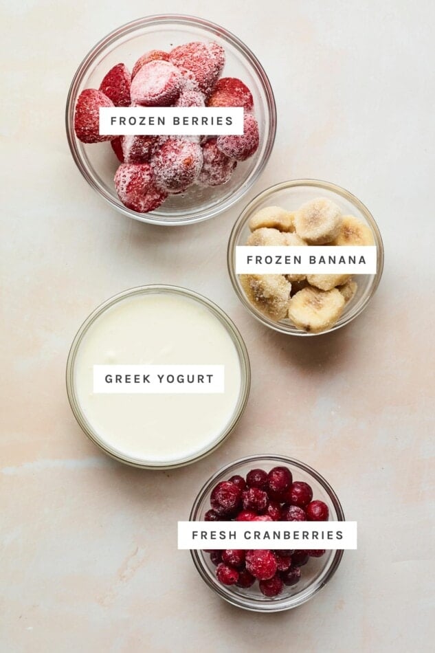 Frozen strawberries, frozen banana, greek yogurt and cranberries measured out into bowls.