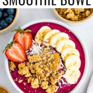 Dragon fruit smoothie bowl topped with granola, banana slices and a strawberry.