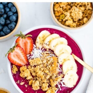 Dragon fruit smoothie bowl topped with granola, banana slices and a strawberry.