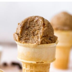 Scoop of oatmeal raisin banana ice cream in a cake cone. Ice cream has a bit taken out of it.