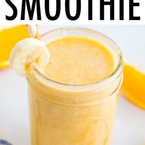 Orange banana smoothie in a glass jar, garnished with a banana slice and served with an orange and white striped paper straw.