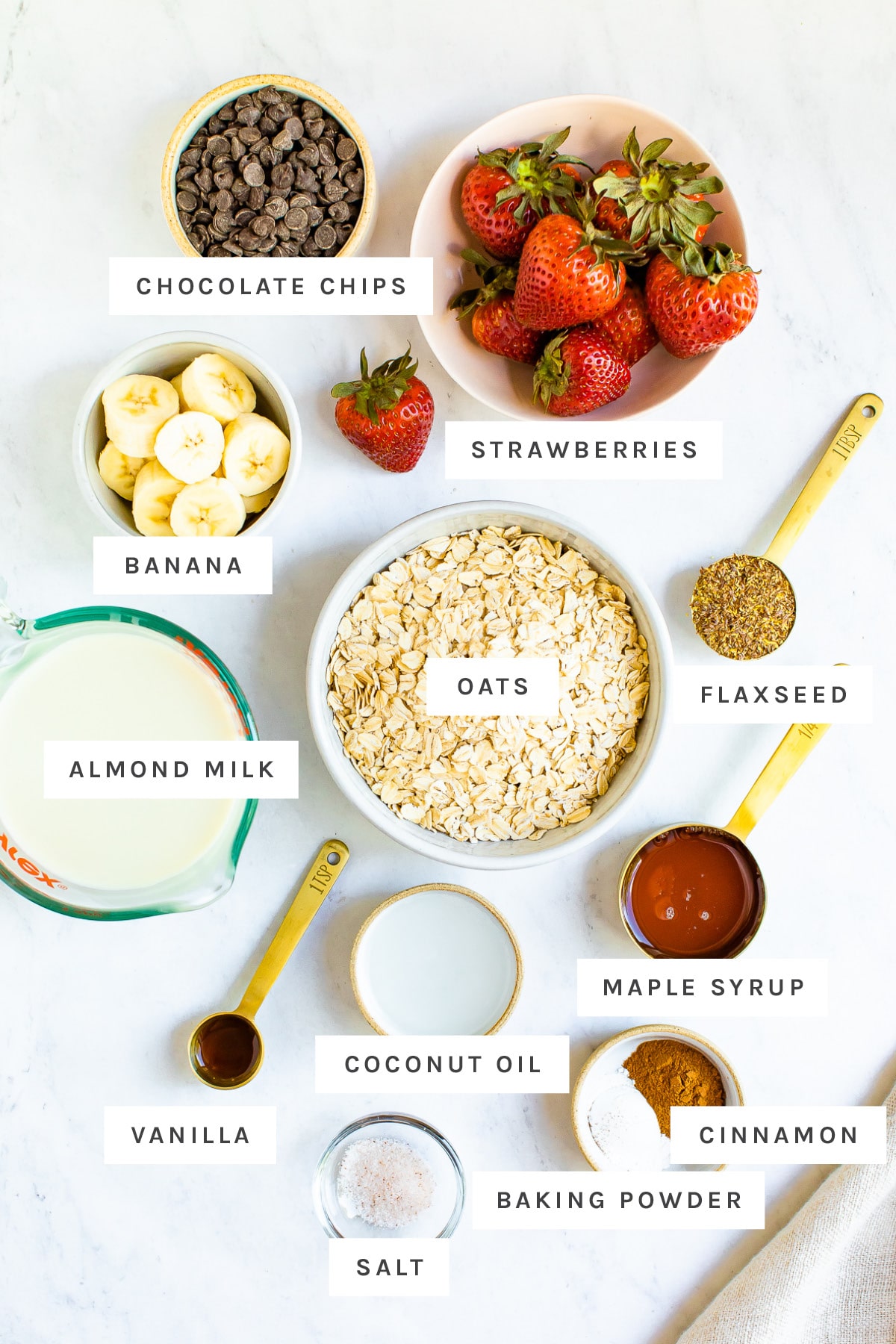 Strawberries, banana, chocolate chips, oats and other ingredients measured out to make strawberry banana baked oatmeal.