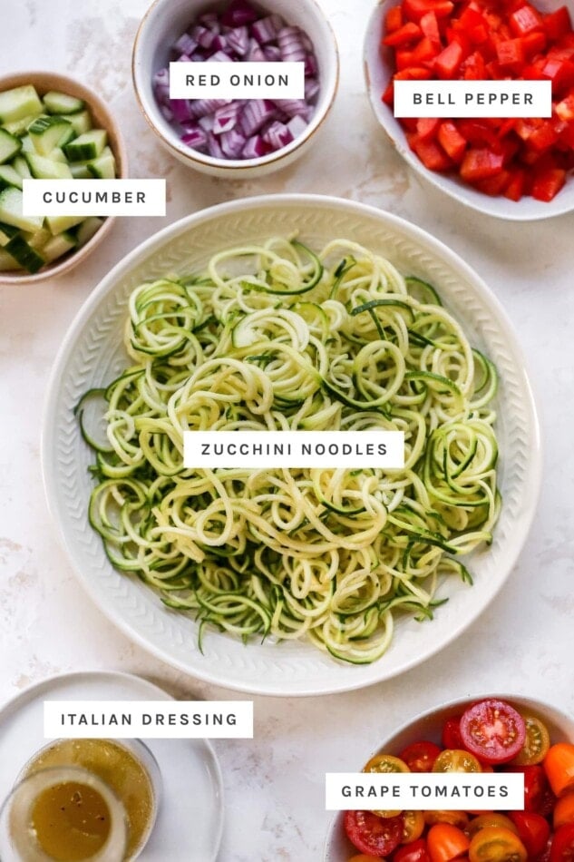 Cucumber, red onion, bell pepper, zucchini noodles, dressing and tomatoes measured out into bowls to make zucchini noodles.