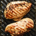 Two well-seasoned chicken breasts on a grill pan with grill marks