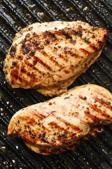 Two well-seasoned chicken breasts on a grill pan with grill marks