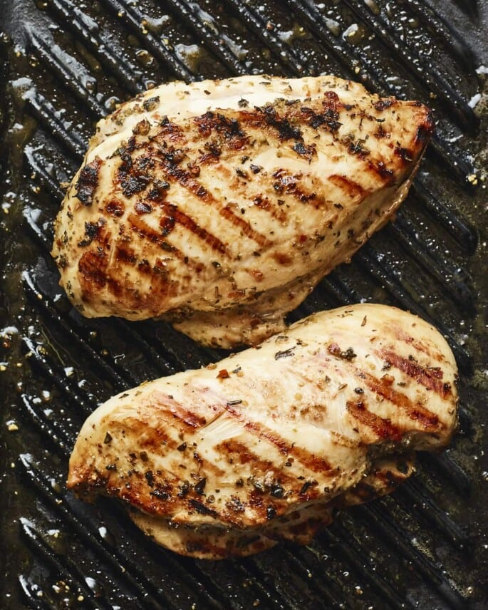 Two well-seasoned chicken breasts on a grill pan with grill marks