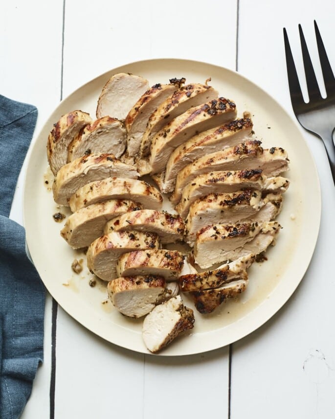 Two chicken breasts cut on a cream colored plate.