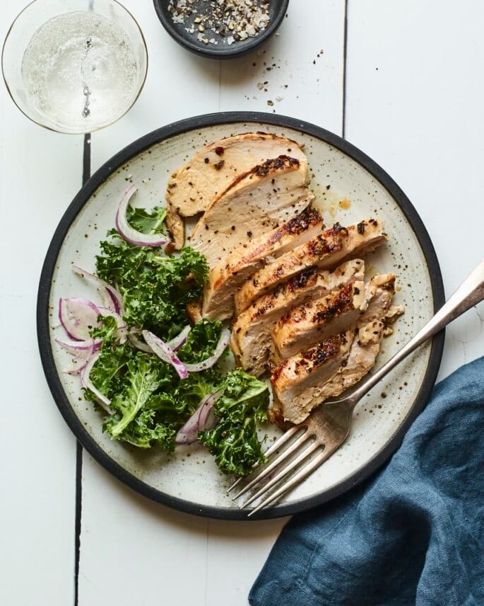 Sliced grilled chicken on a plate with a green salad.