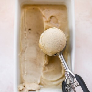 Ice cream scooper scooping a serving of banana ice cream from a loaf pan.