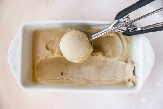 Ice cream scooper scooping a serving of banana ice cream from a loaf pan.