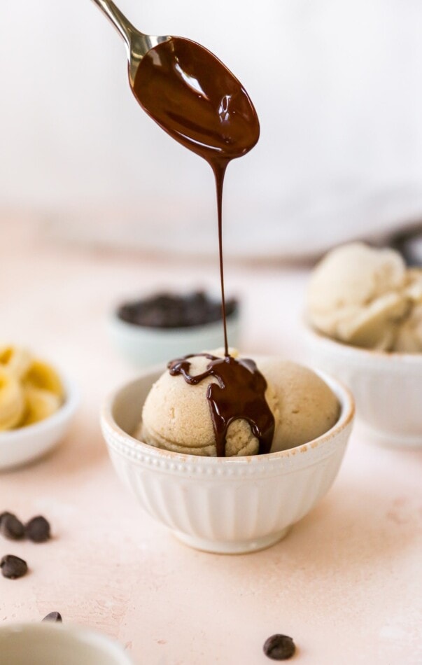 A spoon drizzling homemade magic shell over a bowl of banana ice cream.