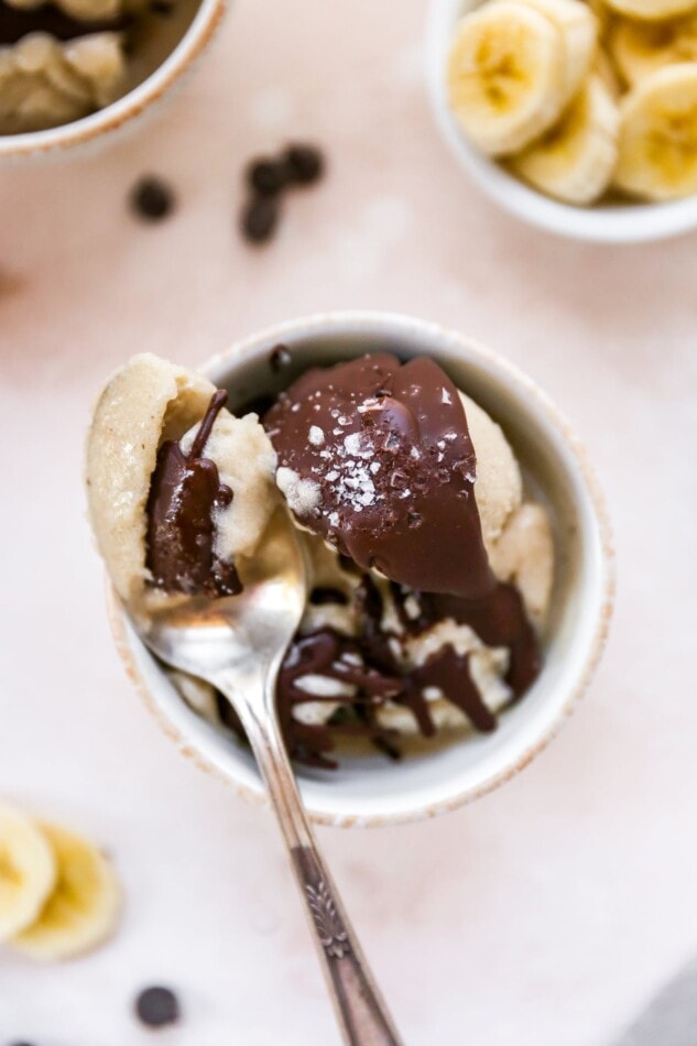 Bowl of banana ice cream topped with homemade magic shell and sea salt. Spoon is taking a bite.