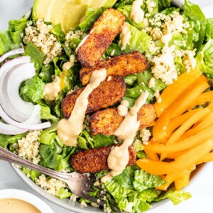 Salad topped with blackened tempeh, tahini dressing, peppers, onions, avocado and quinoa.