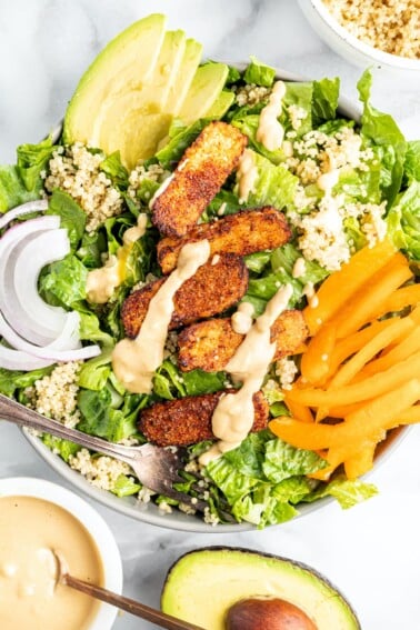 Salad topped with blackened tempeh, tahini dressing, peppers, onions, avocado and quinoa.