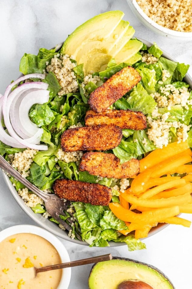 Salad topped with blackened tempeh, peppers, onions, avocado and quinoa.