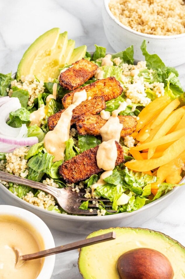 Salad topped with blackened tempeh, tahini dressing, peppers, onions, avocado and quinoa.