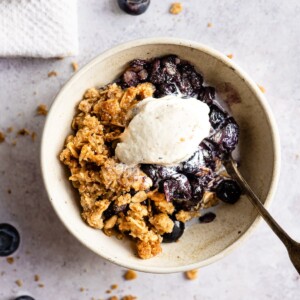 Blueberry crumble topped with vanilla ice cream in a bowl with a spoon.