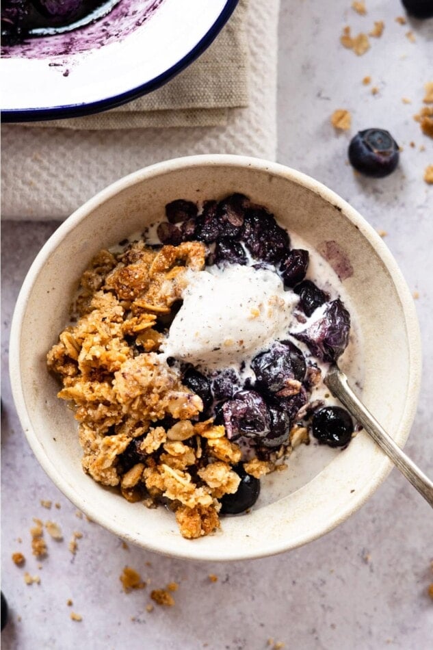 Blueberry crumble topped with vanilla ice cream in a bowl with a spoon.