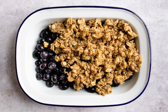 Blueberries in a baking dish getting topped with an oatmeal crumble.