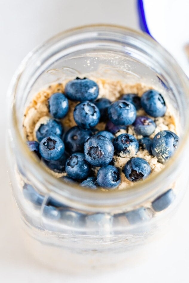 Blueberry overnight oats in a large mason jar with lots of blueberries on top.