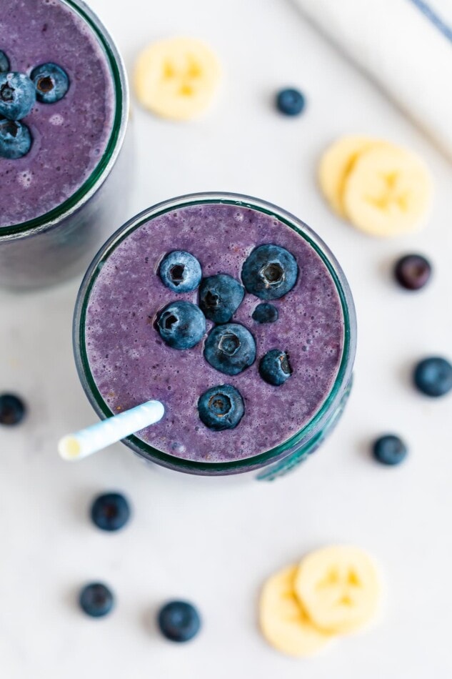 Blueberry smoothie in a glass topped with blueberries and a straw.