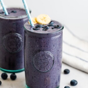 Blueberry smoothie in a glass topped with blueberries, banana slices and a straw.