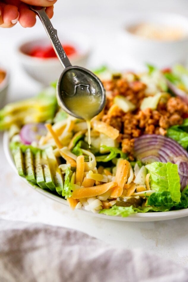 Spoon drizzling honey mustard dressing over a cheeseburger salad.