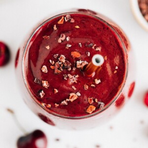 Chocolate cherry smoothie in a glass and topped with cacao nibs and a straw.