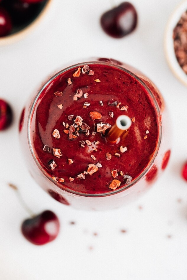 Chocolate cherry smoothie in a glass and topped with cacao nibs and a straw.