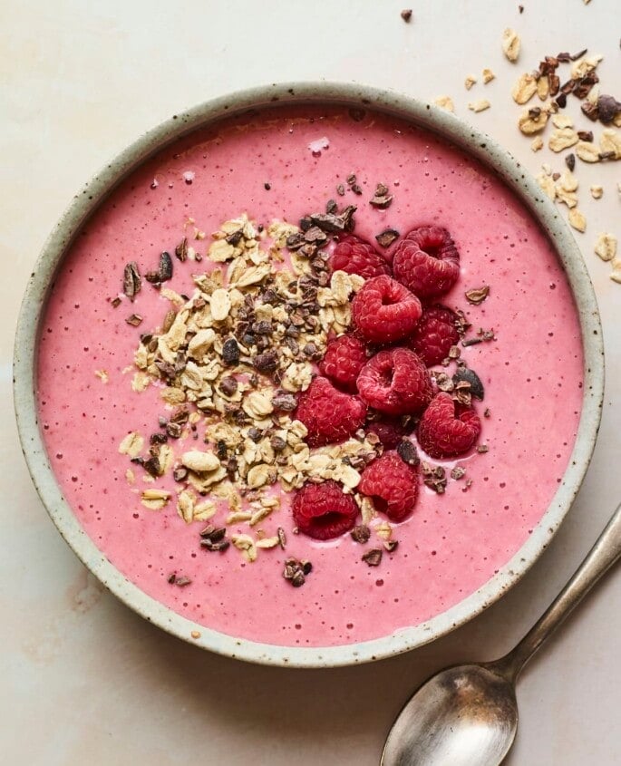 Cranberry smoothie bowl topped with oats, cacao nibs and raspberries.