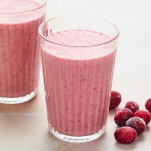 Two glasses of cranberry smoothie. Frozen cranberries are next to the glasses.