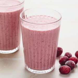 Two glasses of cranberry smoothie. Frozen cranberries are next to the glasses.