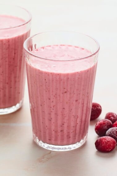 Two glasses of cranberry smoothie. Frozen cranberries are next to the glasses.