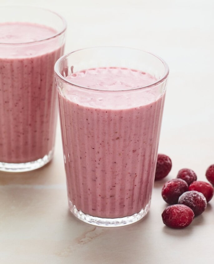 Two glasses of cranberry smoothie. Frozen cranberries are next to the glasses.