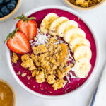 Dragon fruit smoothie bowl topped with granola, banana slices and a strawberry.