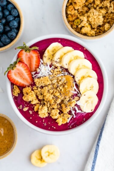 Dragon fruit smoothie bowl topped with granola, banana slices and a strawberry.