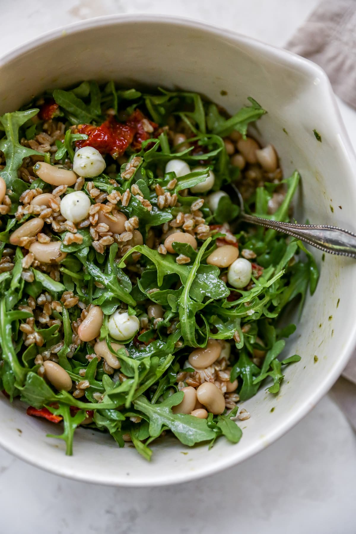 Farro salad with arugula, beans, tomatoes and mozzarella in a mixing bowl with a spoon.