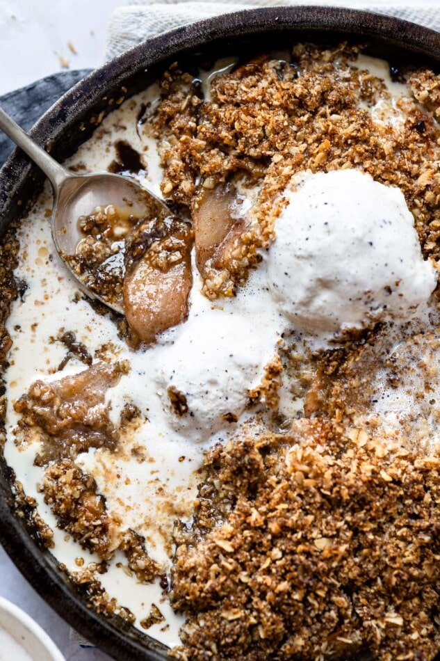 Apple crisp topped with vanilla ice cream. Serving spoon is in the crisp.