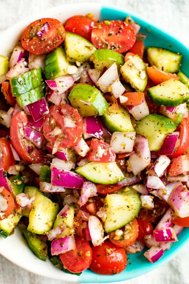 Cucumber tomato and red onion salad in a bowl and seasoned with herbs.