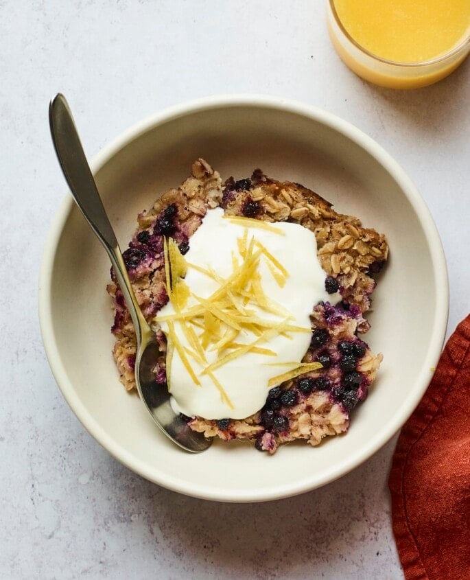 Serving of blueberry lemon baked oatmeal in a bowl and topped with yogurt and lemon zest.