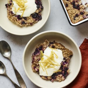 Servings of blueberry lemon baked oatmeal in two bowls and topped with yogurt and lemon zest.